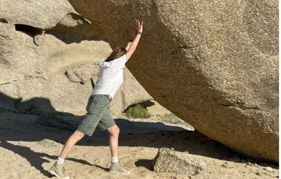 Eine Person stemmt sich spielerisch gegen einen großen Felsbrocken