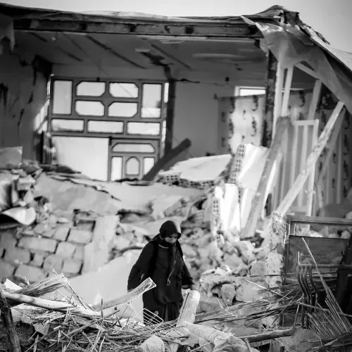A woman walks through the rubble of a collapsed house