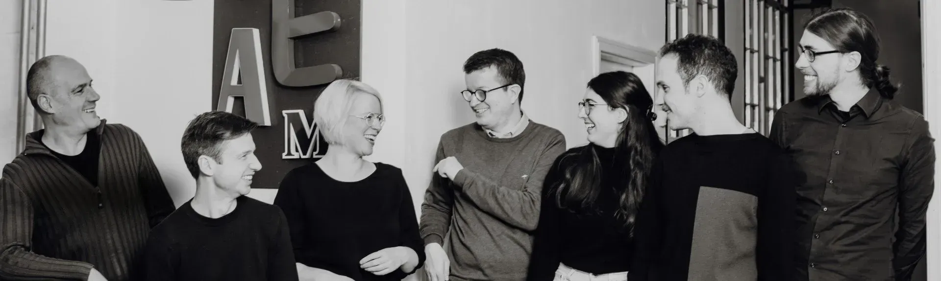 Aufnahme von einem Teil des Effektiv Spenden Teams. Alle sieben Personen schauen sich lachend gegenseitig an. 
