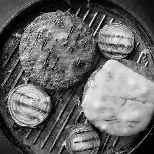 Pflanzenbasierte Patty und Käsescheibe auf einem Grill neben Zwiebelringen