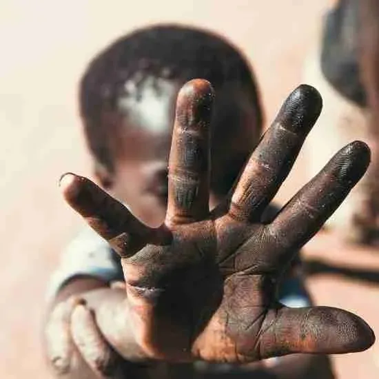 A child holds out a dirty hand toward the camera