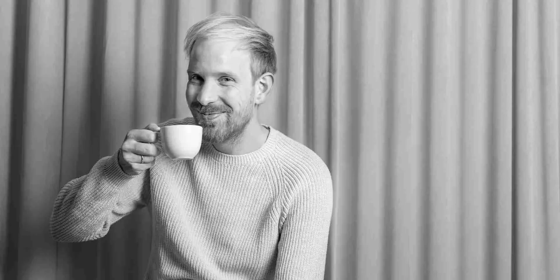 Foto von Rutger Bregmann, der in die Kamera lächelt und eine Tasse zum Mund hebt. 