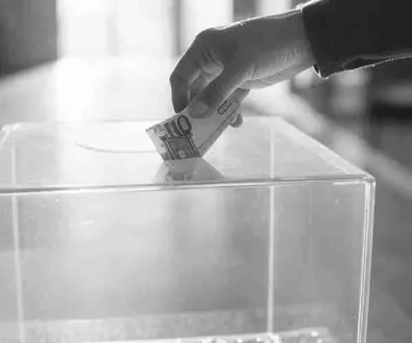 Hand dropping a banknote into a transparent donation box