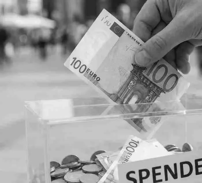 Eine Hand wirft einen 100-Euro-Schein in eine Spendenbox