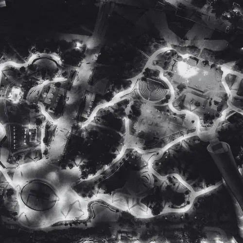 Schwarz-weiße Nachtluftaufnahme eines beleuchteten Parks mit geschwungenen Wegen