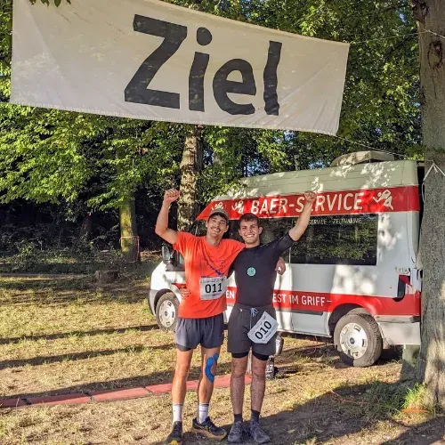 Manuel Hillenmeyer jubelt mit einem Mitläufer unter dem Zielbanner eines Laufs