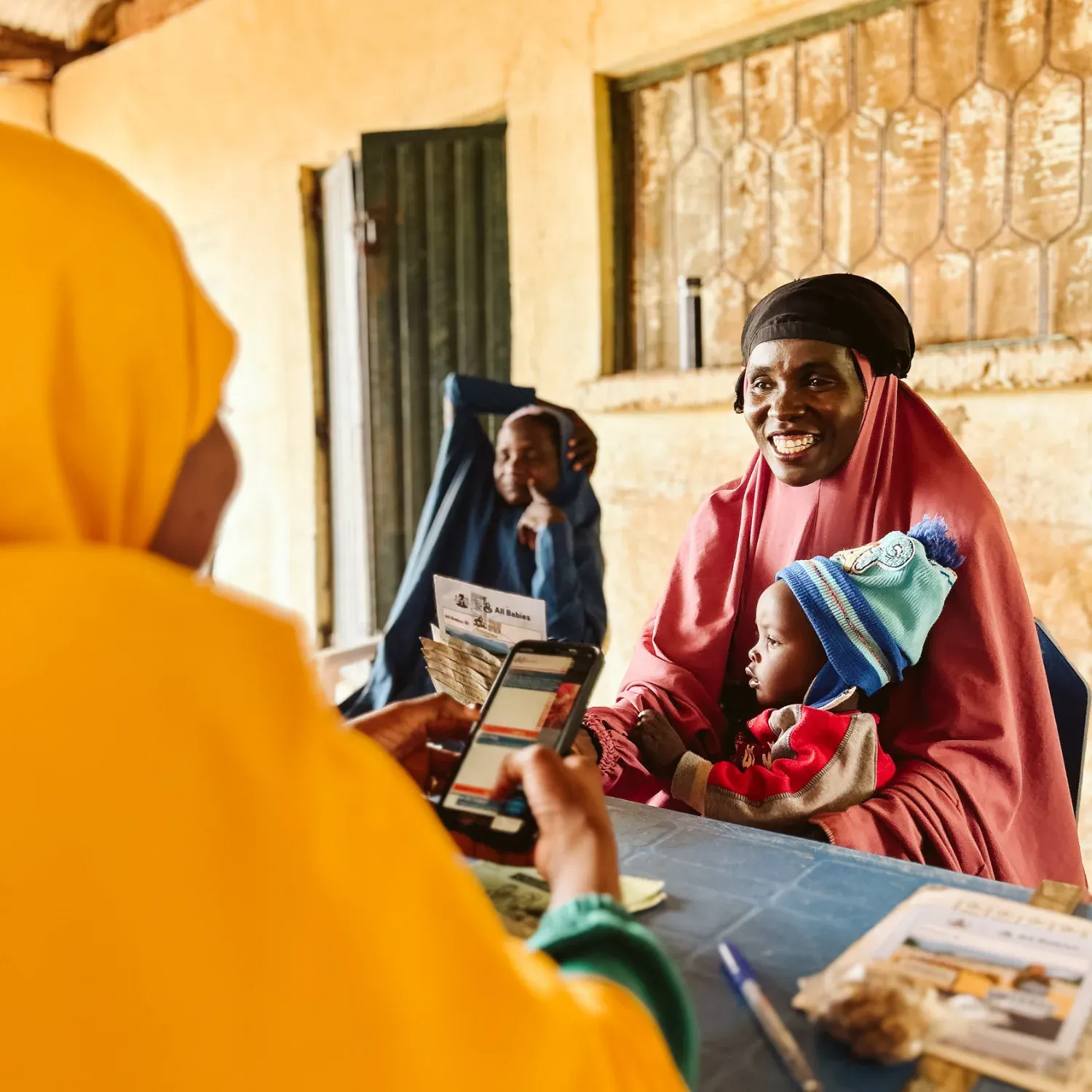 Eine Mutter mit ihrem Kind erhält bei einer Impfklinik in Nigeria eine Geldüberweisung per Smartphone