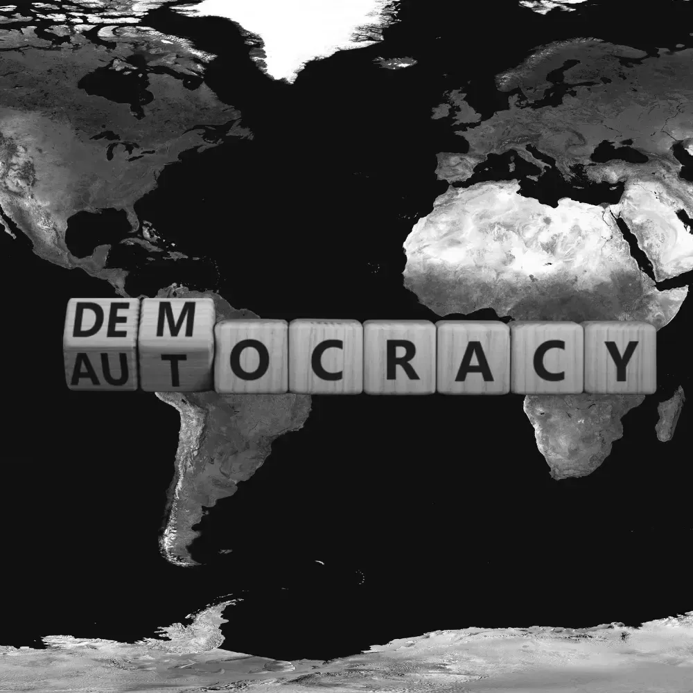 Buchstabenwürfel auf einer Weltkarte formen das Wort „Democracy“, das sich in „Autocracy“ verwandelt