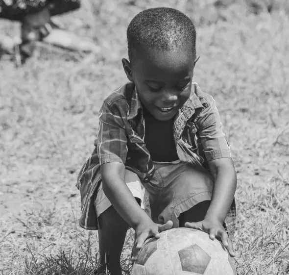 Young boy crouching and laughing with a football in a field