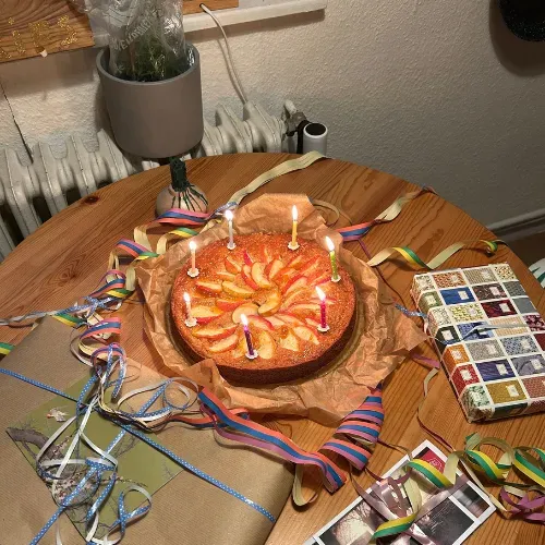 Ein Geburtstagskuchen mit brennenden Kerzen, umgeben von Geschenken und Luftschlangen