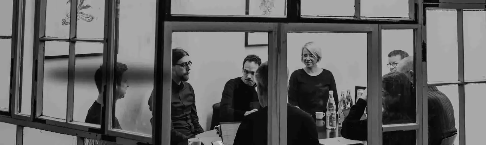 Shot through a window wall of the Effective Donations team sitting around a table and talking. 