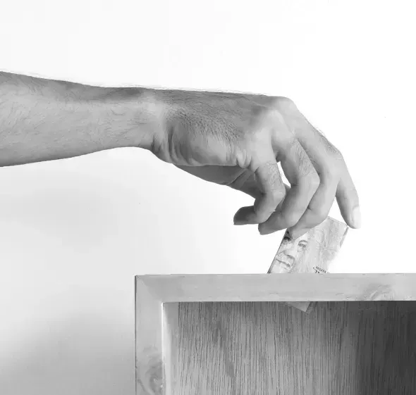 A hand drops a banknote into a donation box